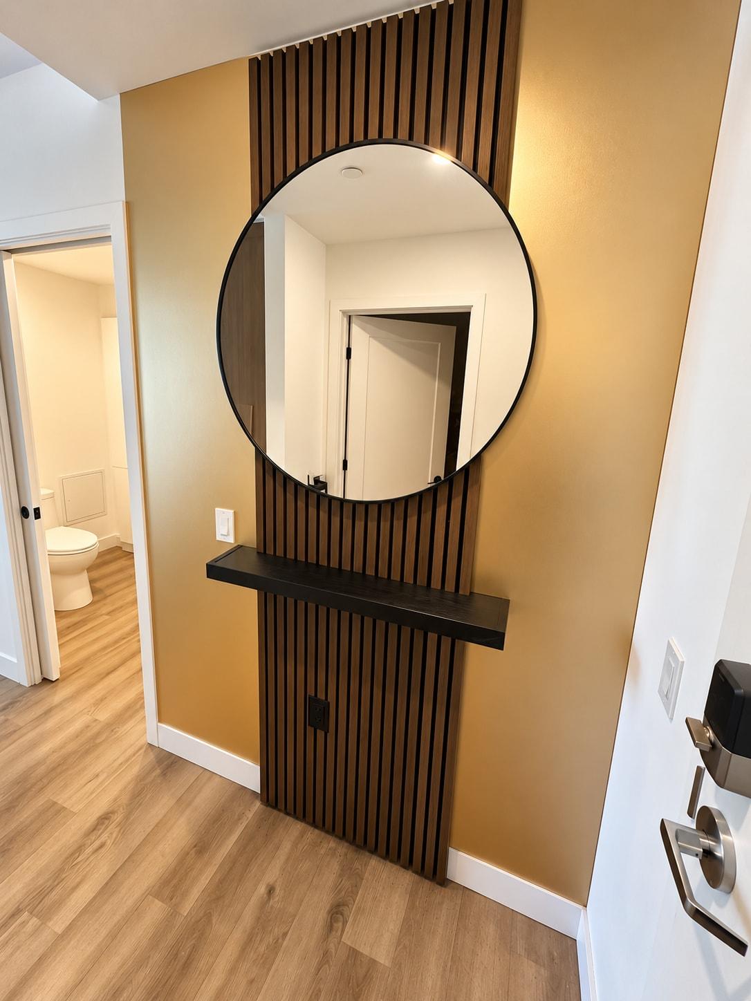 L’entrée : mur doré, lattes de bois noir et grand miroir rond