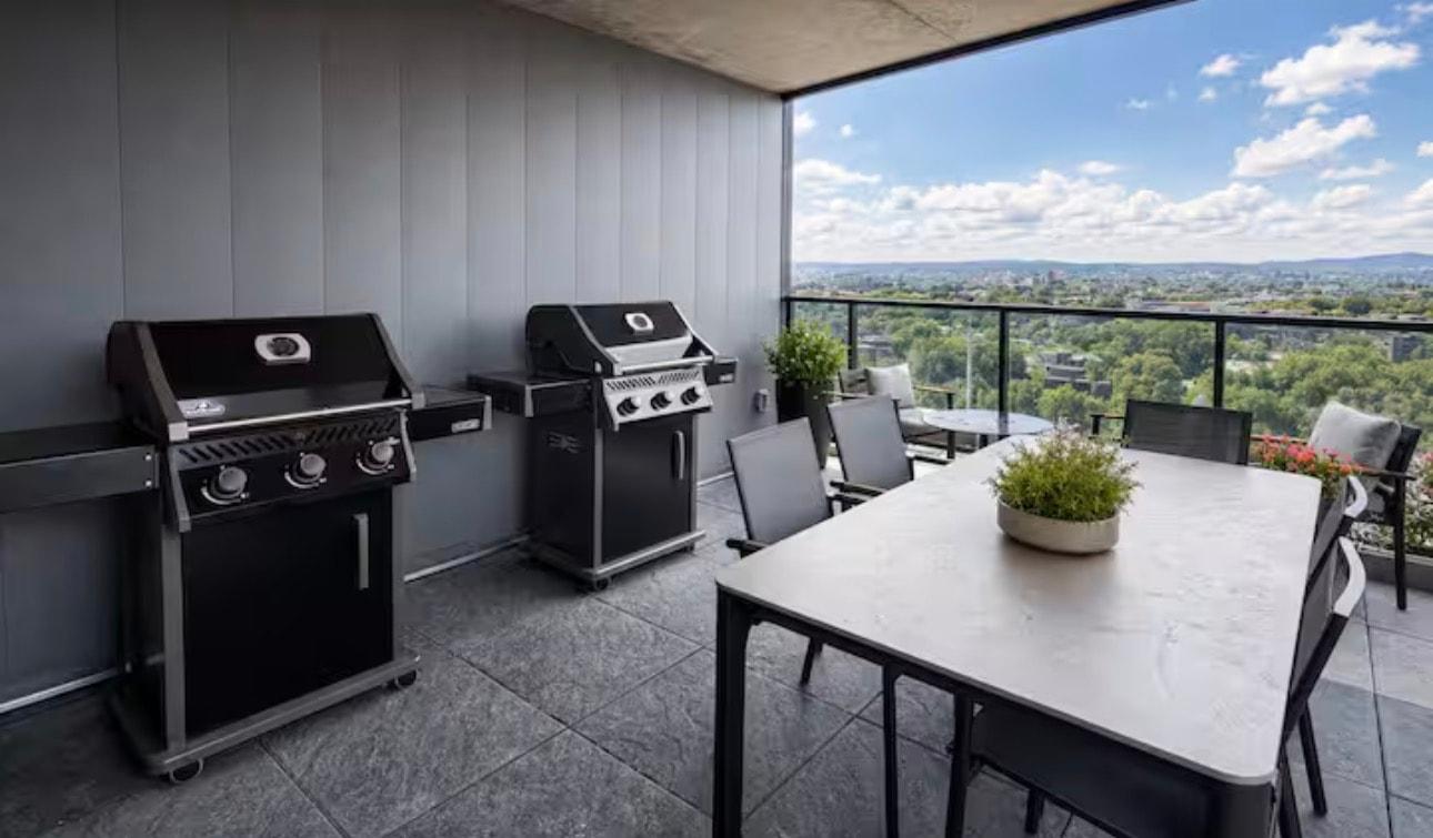 Terrasse couverte avec deux barbecues et une grande table, vue sur la ville